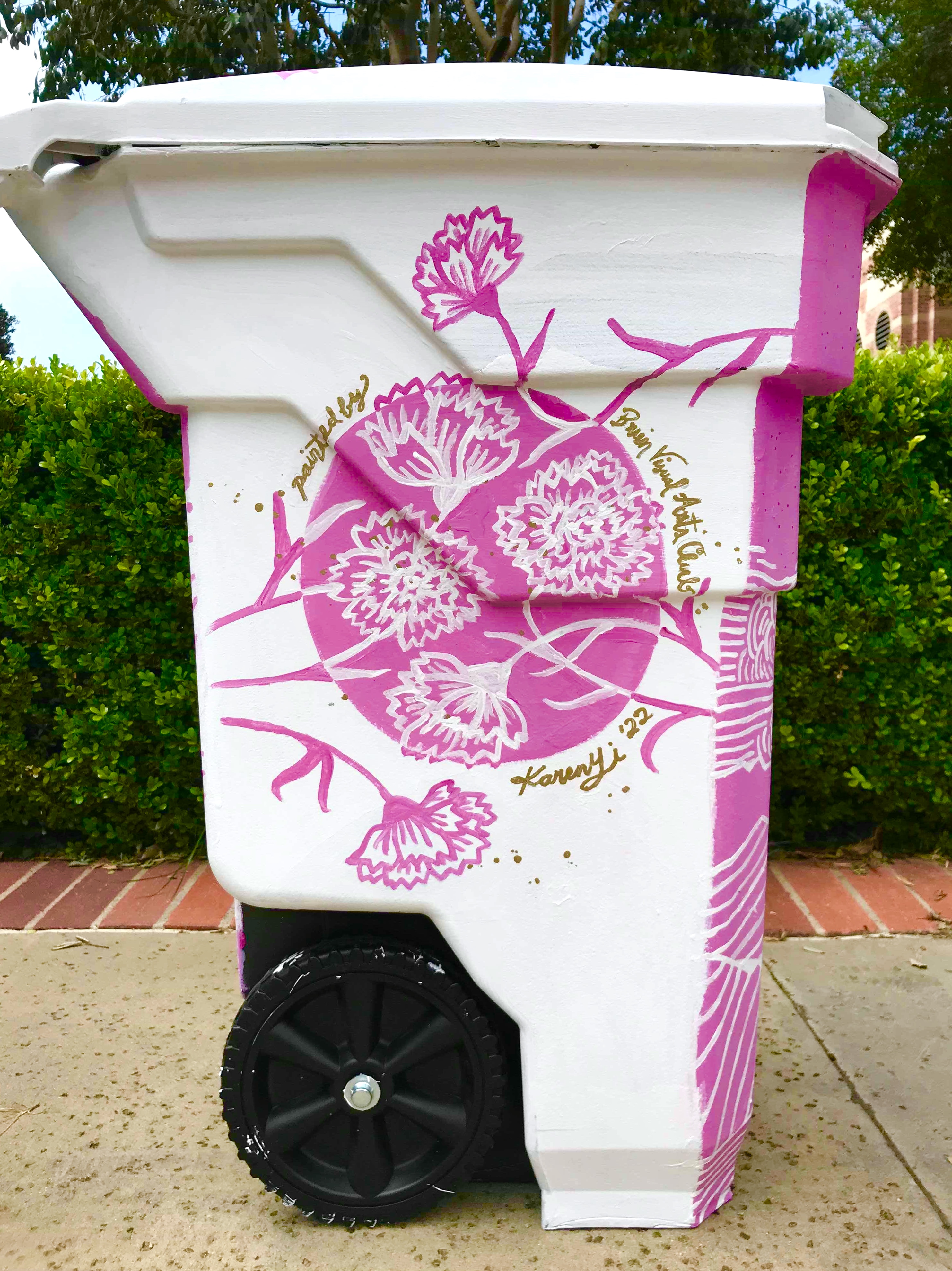 Trash can painted in white with pink carnations and gold text saying Painted by Bruin Visual Arts Club