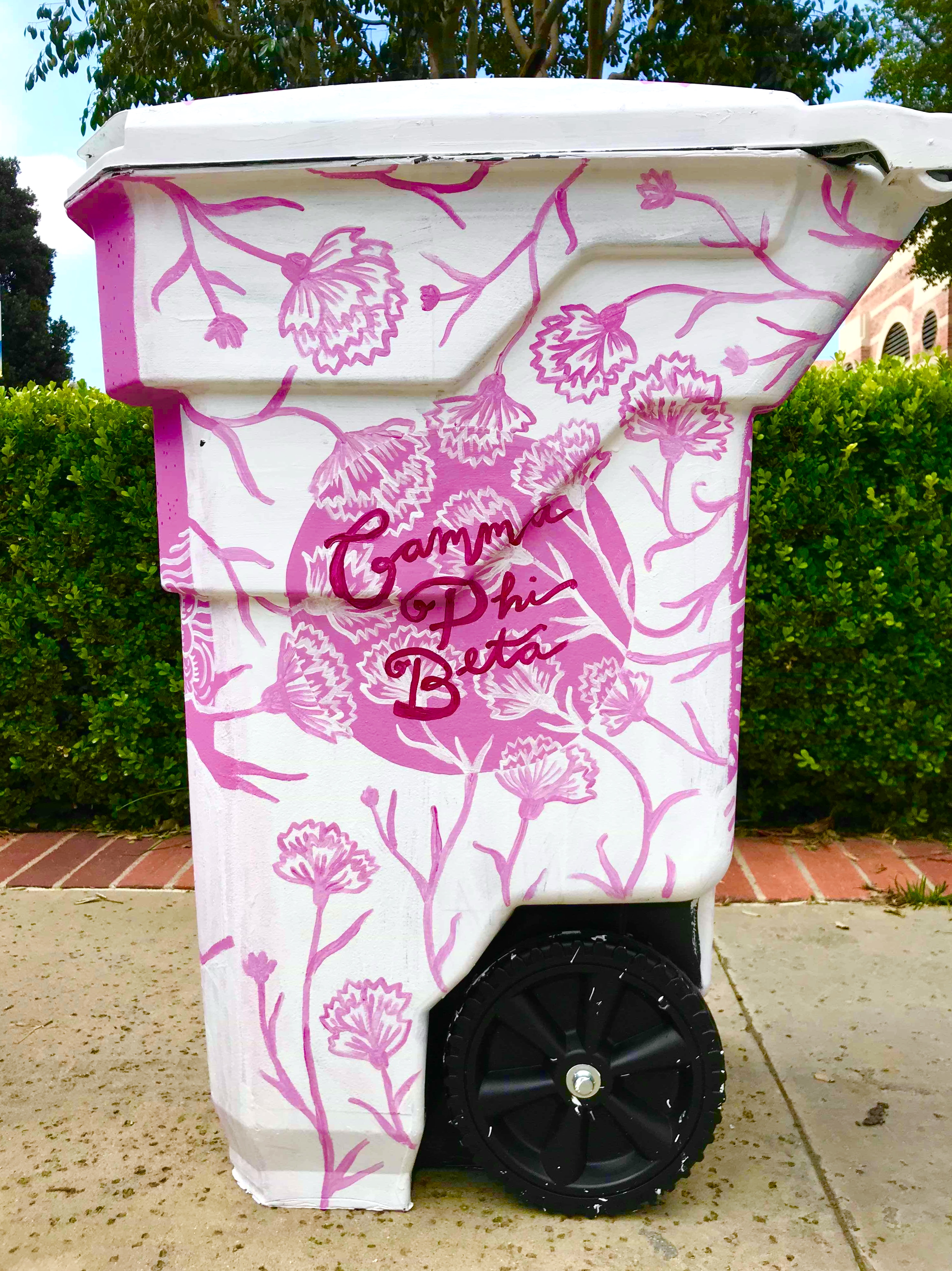 Trash can painted in white with pink carnations and magenta cursive text saying Gamma Phi Beta