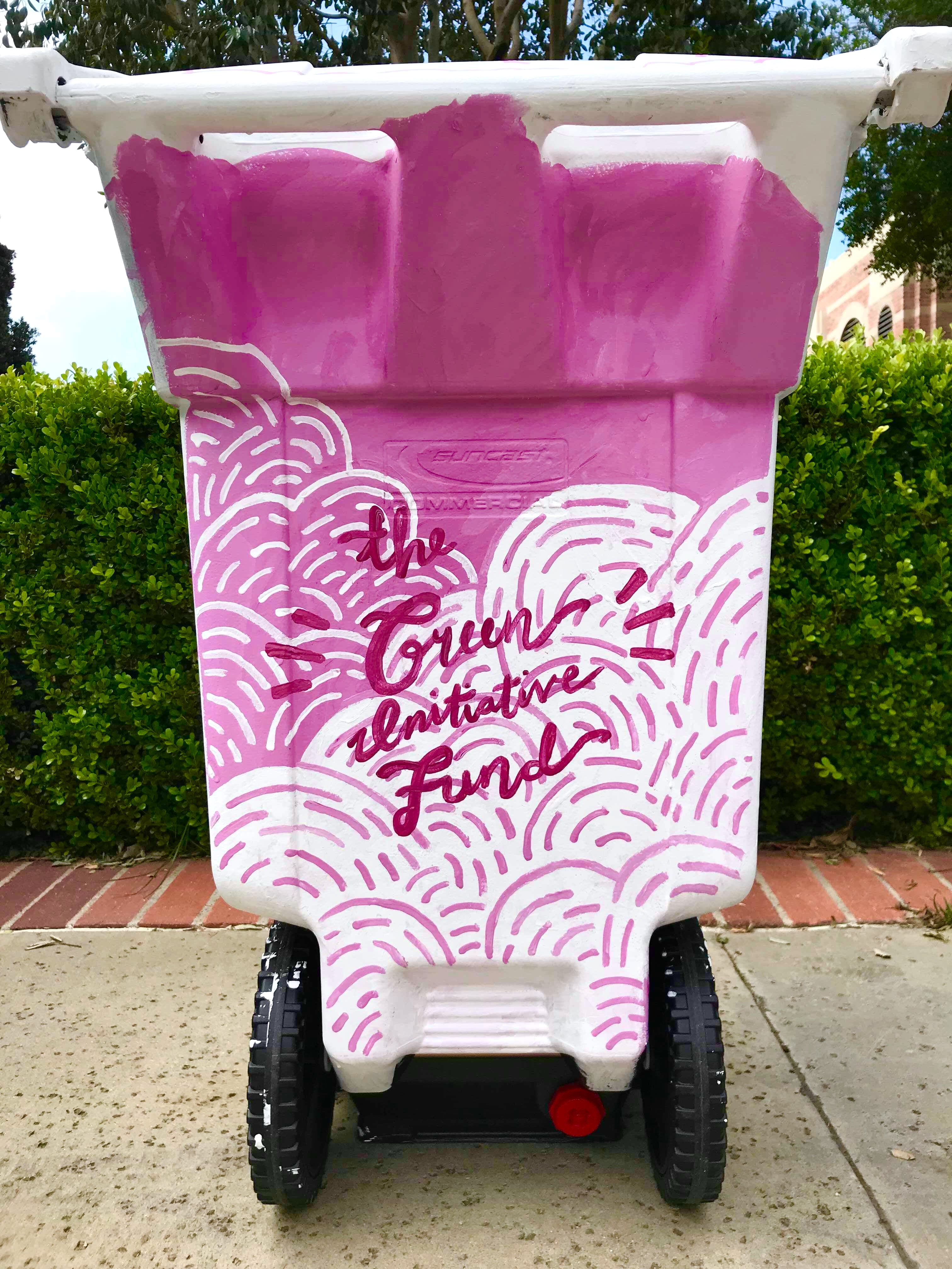 Trash can painted in pink with white mountains and magenta cursive text saying The Green Initiative Fund